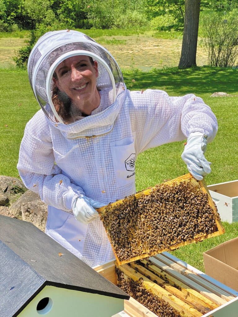 Darcy Huda in beekeeping gear with a honeycomb frame