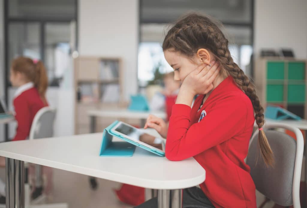 Schoolgirl using digital tablet during lesson in classroom at primary school. Increased time indoors, especially including screen time, is a factor in the development of childhood myopia.