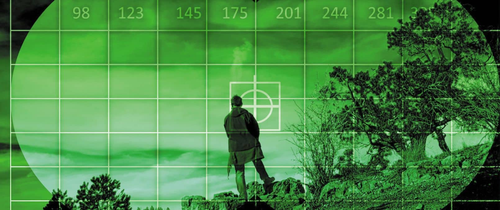 Night vision technology view through a night vision device, showing a person standing on rocky terrain with trees in the background. The image is green-tinted with a grid overlay, typical of night vision imagery.