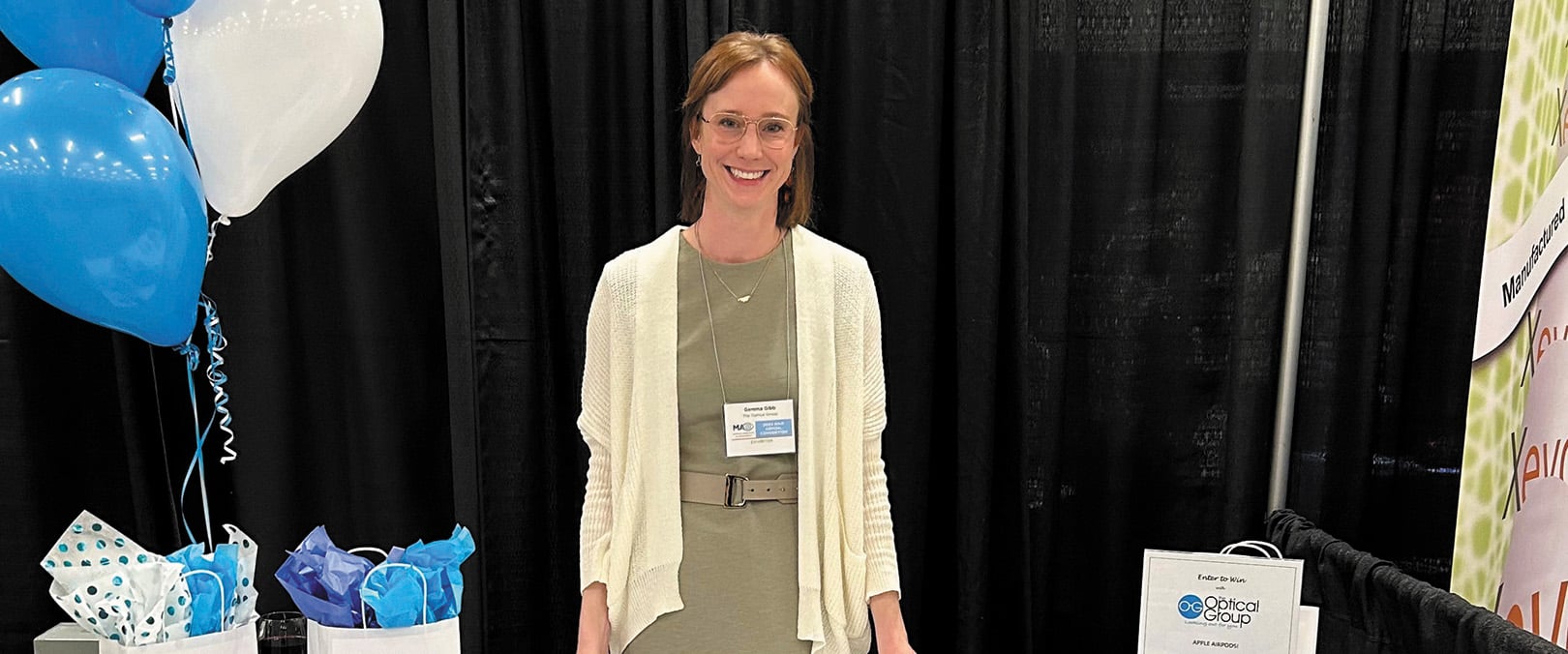 Gemma Gibb standing in front of a tradeshow booth for the Optical Group.